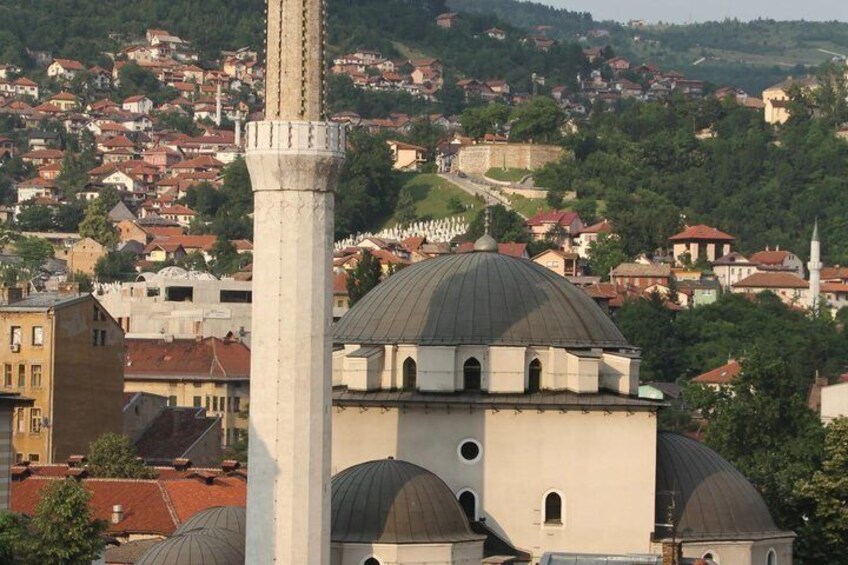 A mosque with a tall minaret and domes, surrounded by a densely packed town with red-roofed houses. 5