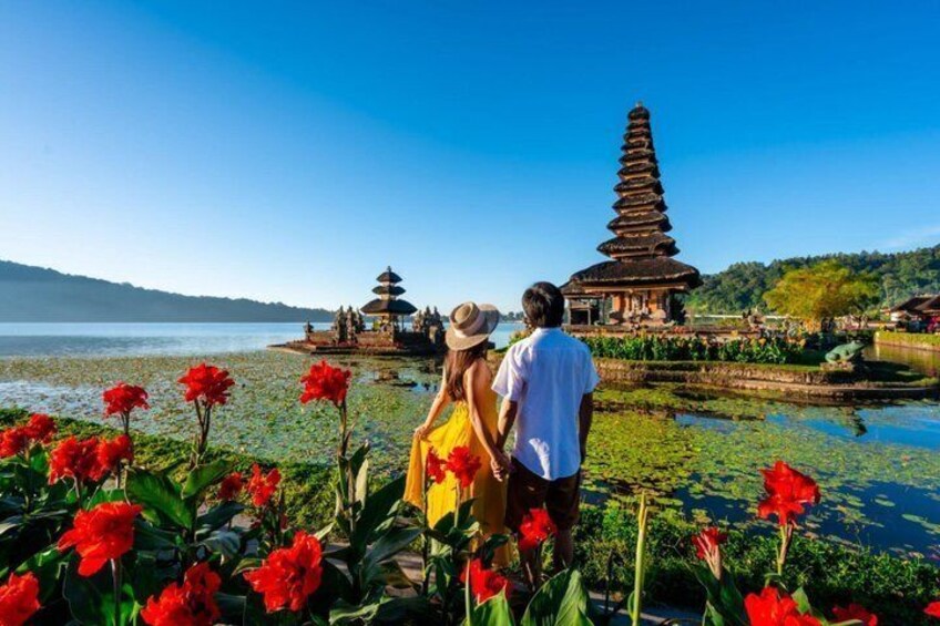 A couple walking by a temple with a lotus pond and red flowers. 1