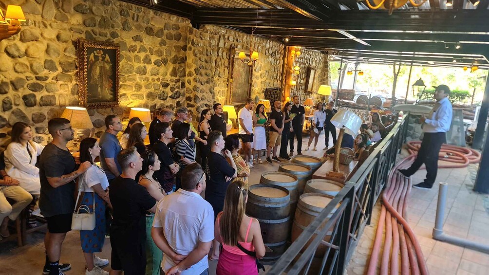 A crowd inside a stone-walled building with wooden barrels and hanging lamps. 4