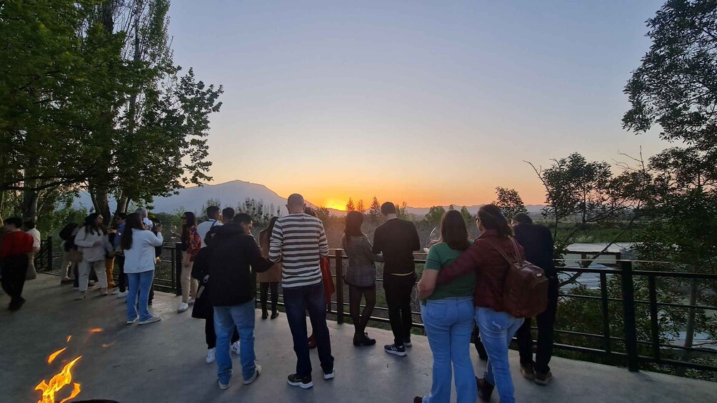 A group of people standing on a bridge, overlooking a sunset with mountains in the background. 2