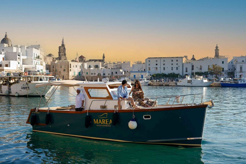 A boat named 'MAREA' docked at a marina with buildings and a tower in the background. 1