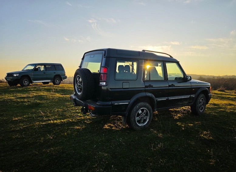 A black SUV parked on a grassy field with a sunset in the background. 3