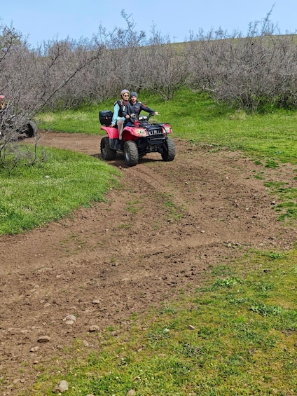 Two people on a red ATV on a dirt path surrounded by sparse vegetation. 2