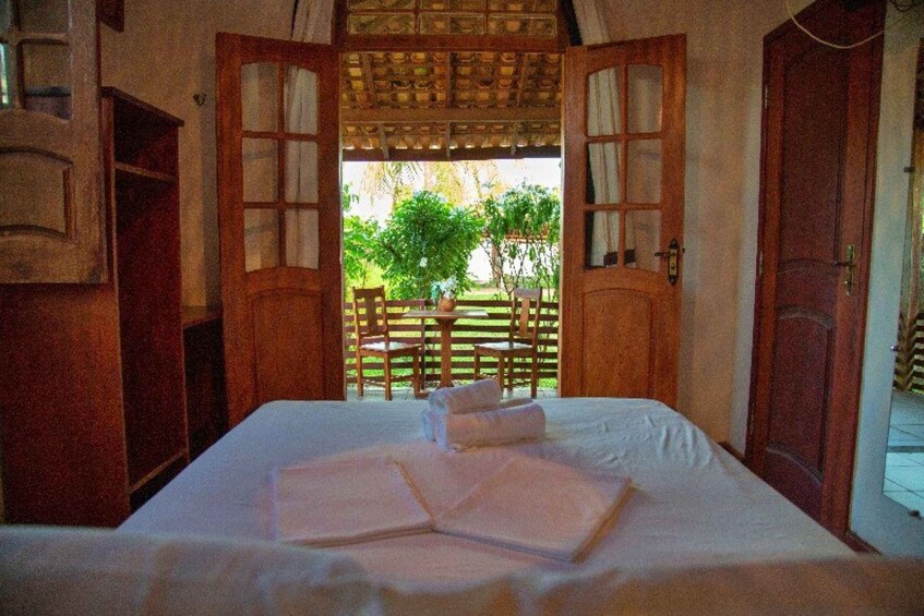 A bed with towels, a wooden door, and a view of a garden. 3