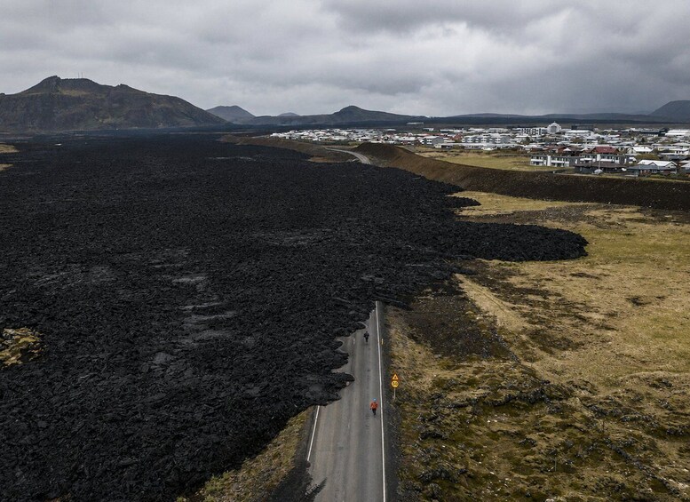 A road winding through a volcanic landscape with a small settlement in the distance. 3