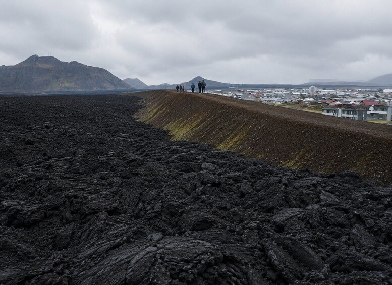 A volcanic landscape with a lava field, a small settlement, and distant mountains. 1