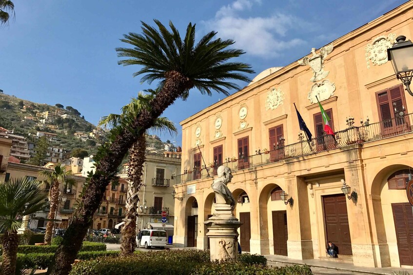 A historic building with a statue, palm trees, and a mountainous backdrop. 4