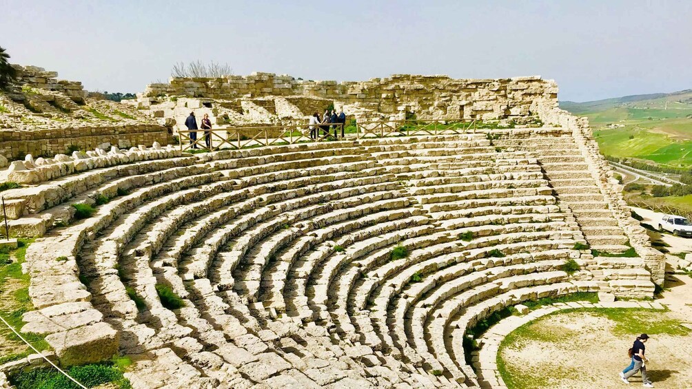 An ancient amphitheater with stone seating and a few visitors. 5