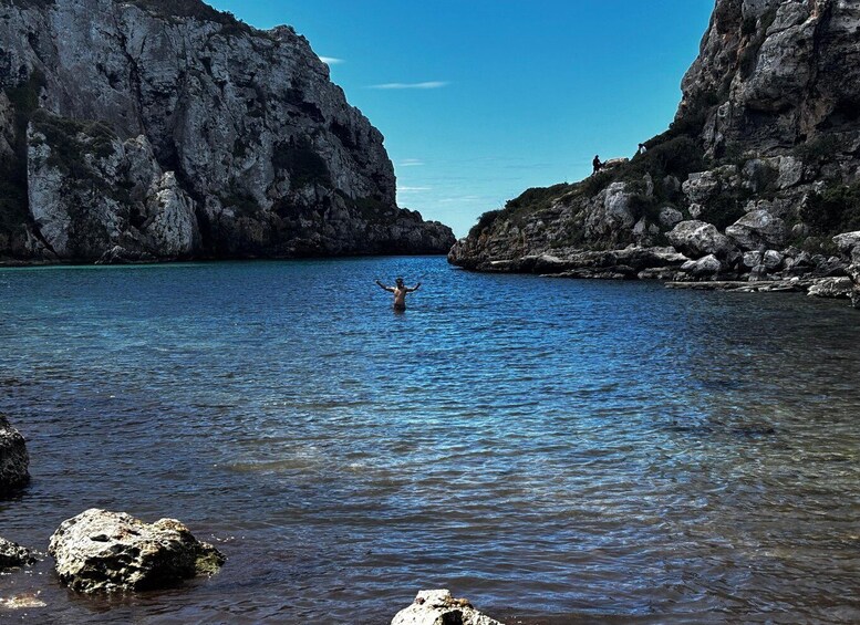 A person standing in a clear blue body of water surrounded by rocky cliffs. 2