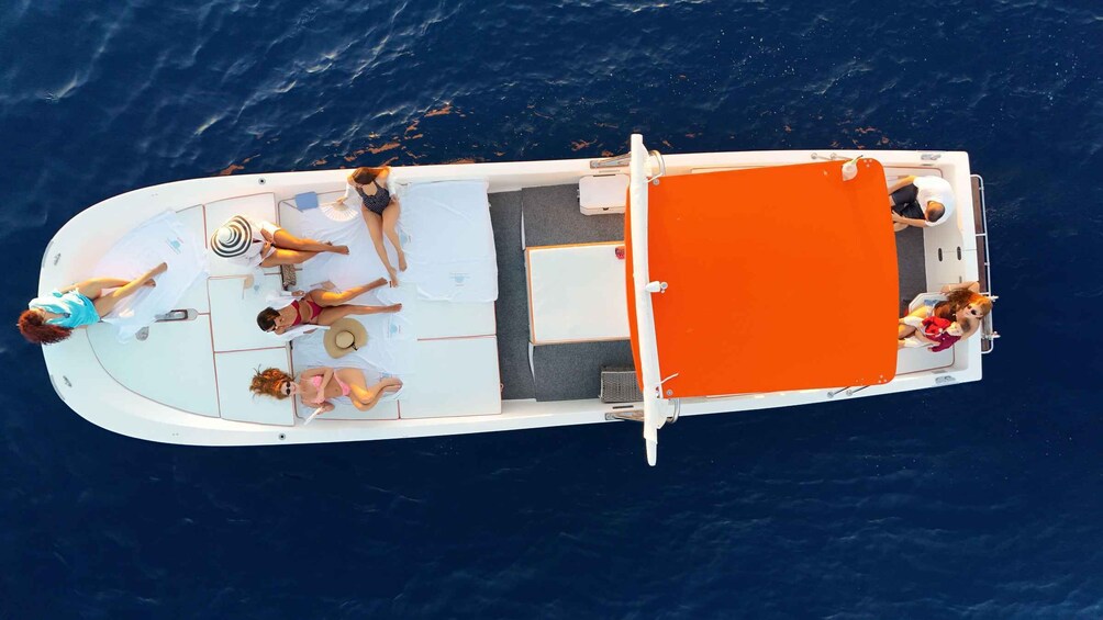 A white boat with an orange deck, people sunbathing, and a child with a doll. 2