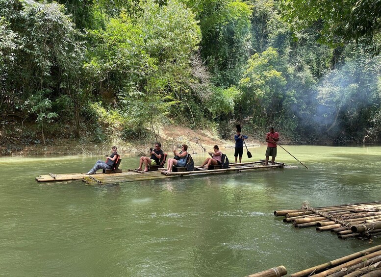People on a bamboo raft in a river surrounded by dense forest. 1