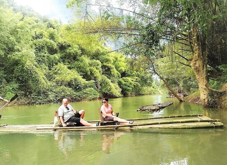 Two people sitting on a bamboo raft in a calm river surrounded by dense greenery. 5