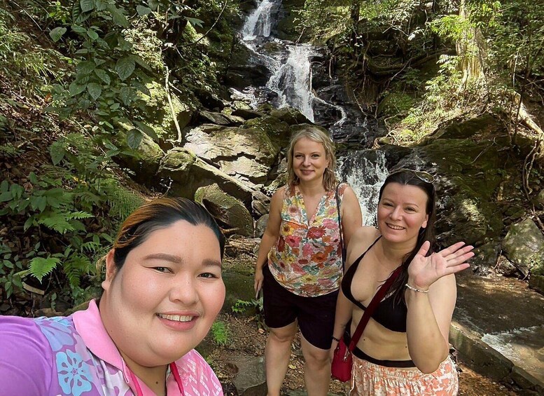 Three people standing in front of a waterfall surrounded by greenery. 2