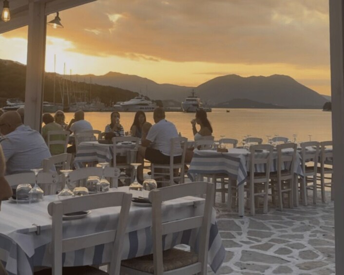 A seaside restaurant with tables and chairs, overlooking a calm body of water with boats and mountains in the background. 5