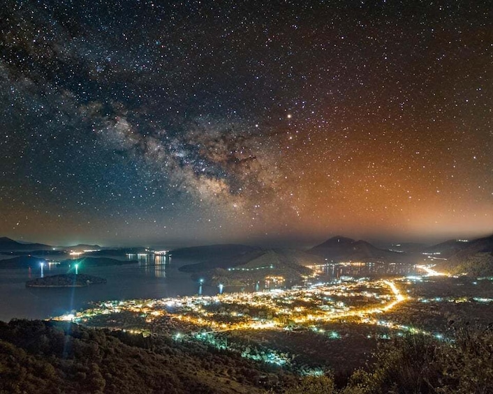 A starry night sky over a coastal city with a bridge and illuminated buildings. 1