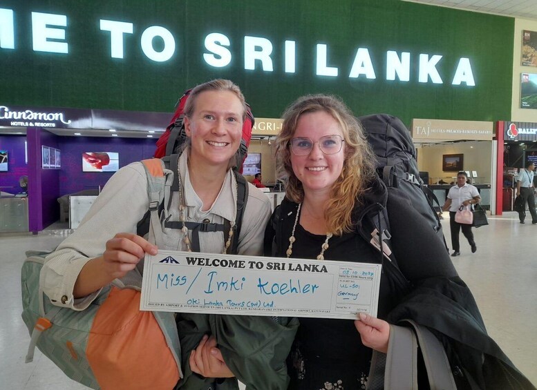Two people holding a welcome sign at an airport with a 'Welcome to Sri Lanka' sign in the background. 3