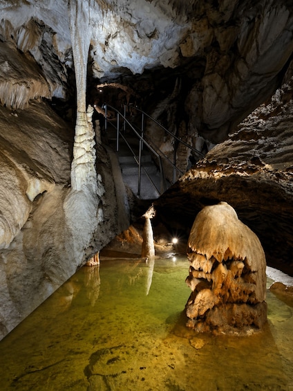 A cave with stalactites, stalagmites, and a water pool. 1