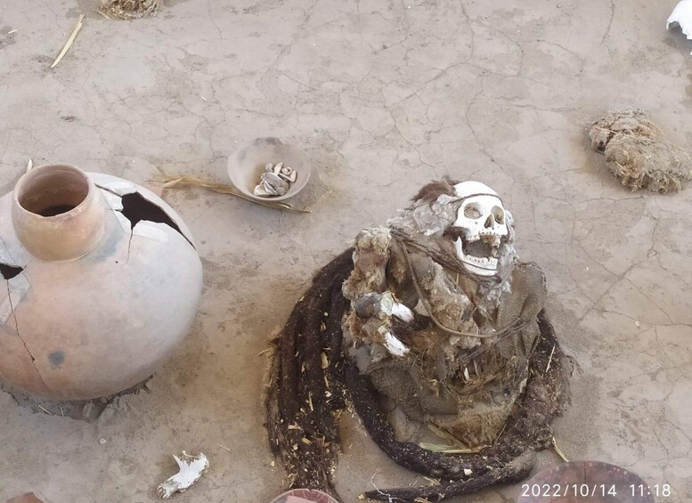 A skeleton with a skull, surrounded by a broken clay pot and a small dish with bones. 2