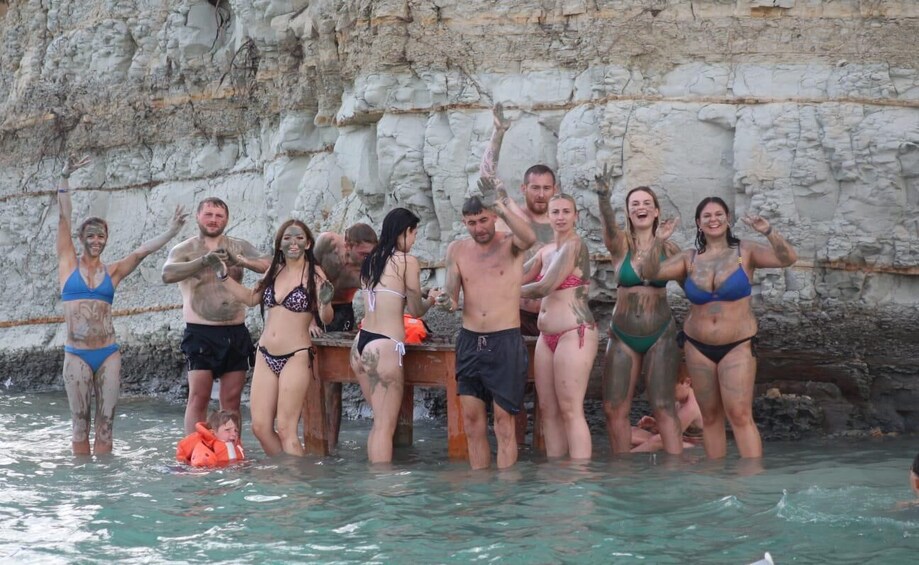 A group of people in a natural water setting with rocky cliffs in the background. 1
