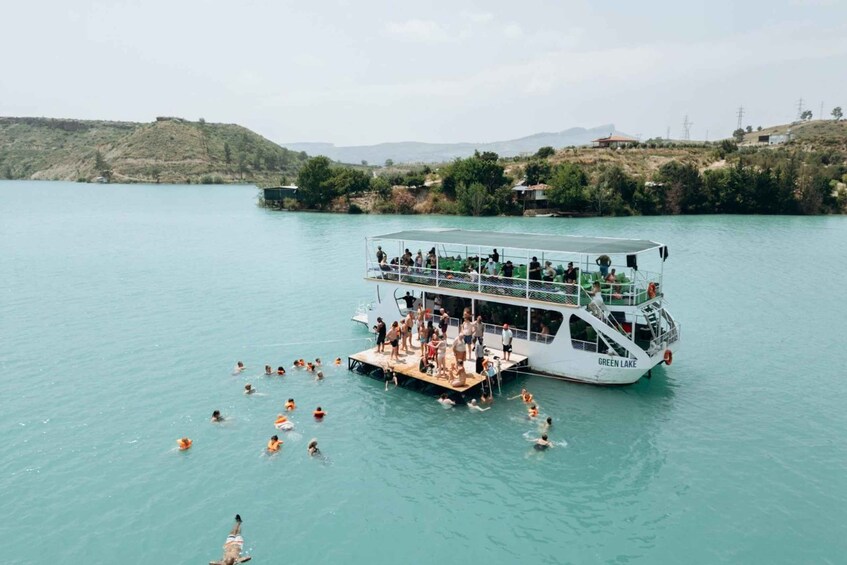 A boat named 'GREEN LAKE' with people swimming in the water and a dock. 3