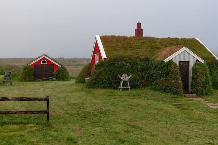 A rural landscape with a red barn, a white shed, and a thatched-roof structure on a grassy hill. 2