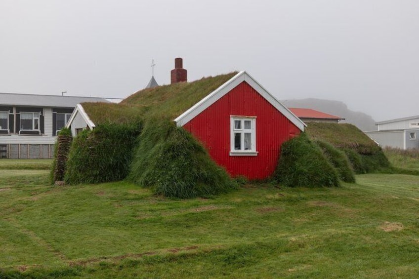 A red house with a grass-covered roof, surrounded by green grass and a cloudy sky. 3