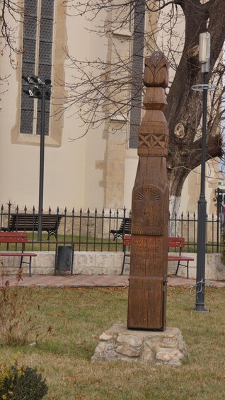 A wooden sculpture in a park with benches and a fence in the background. 3