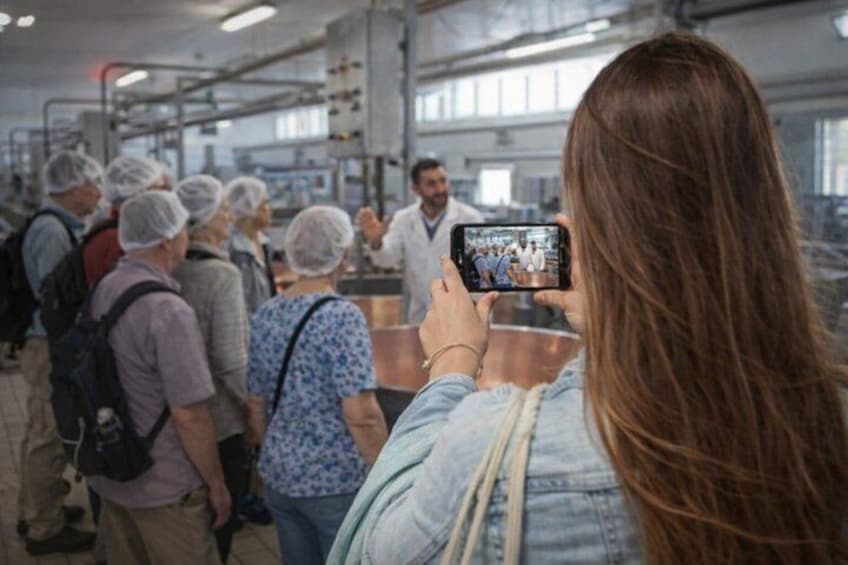 A group of people in a factory setting, some wearing hairnets, and one person taking a photo. 1