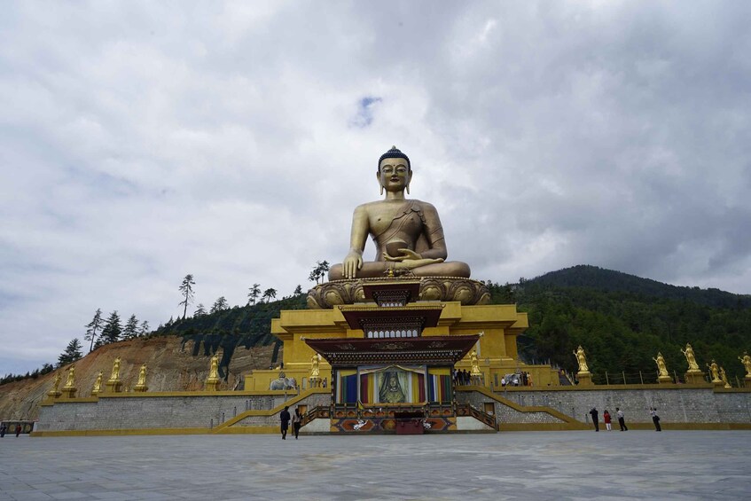 A large seated Buddha statue with a golden base, surrounded by a yellow-roofed structure and smaller golden statues. 1
