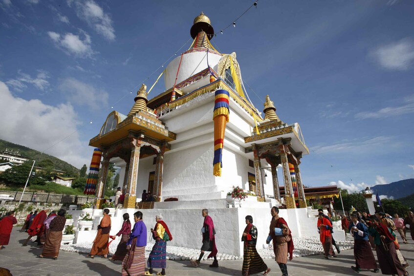 A white stupa with golden accents and colorful flags, surrounded by people in traditional attire. 4