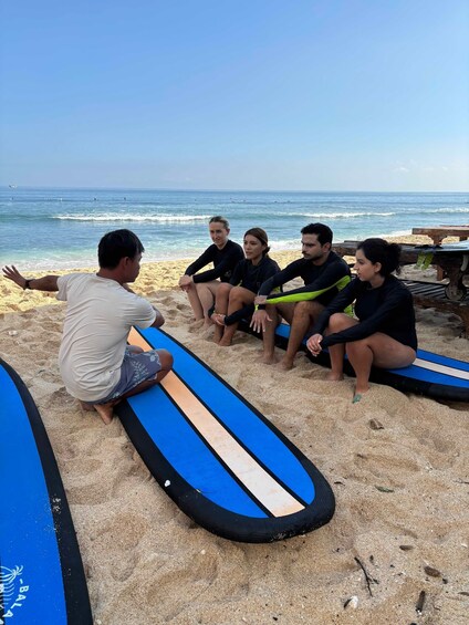 A group of people sitting on surfboards on a sandy beach with the ocean in the background. 2