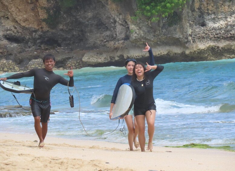 Three people in wetsuits walking on a sandy beach with ocean waves in the background. 3