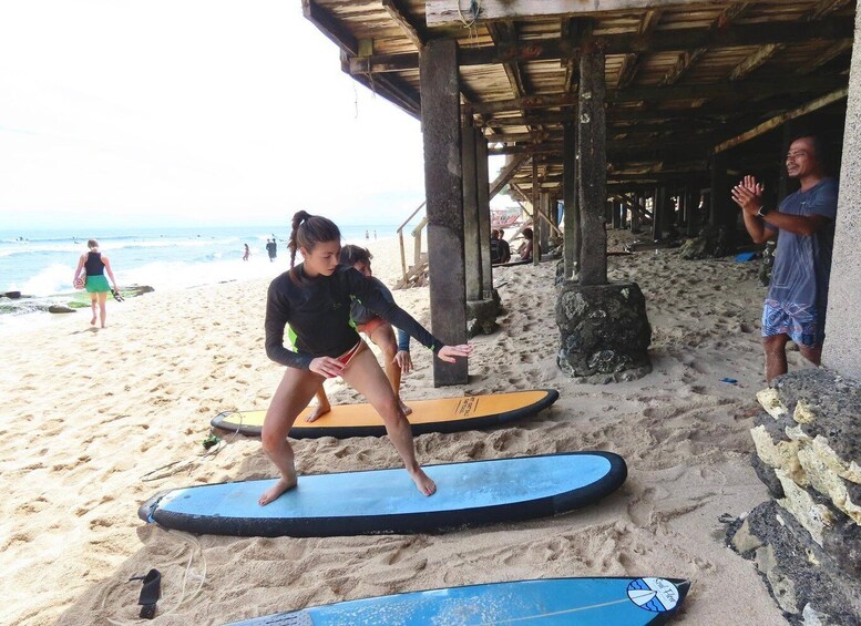 A person practicing on a surfboard at a beach with a wooden structure in the background. 5