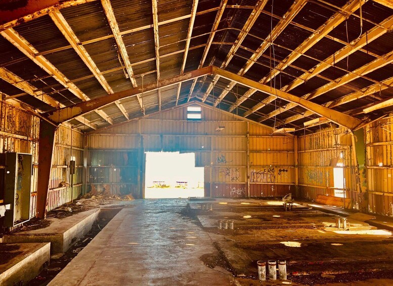An abandoned industrial building with a high ceiling, metal beams, and graffiti on the walls. 1