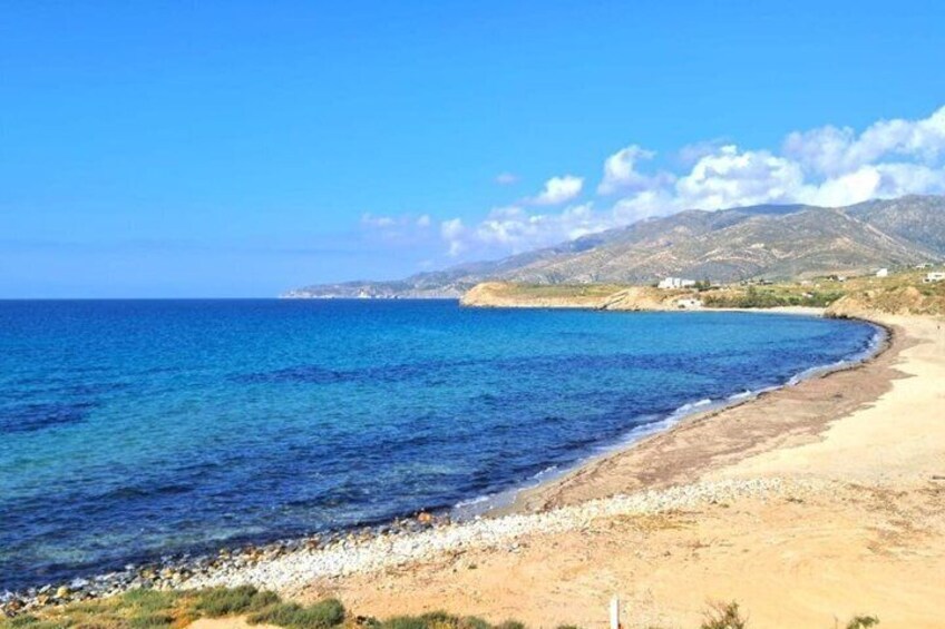 A coastal beach with clear blue waters, a sandy shore, and distant mountains. 2