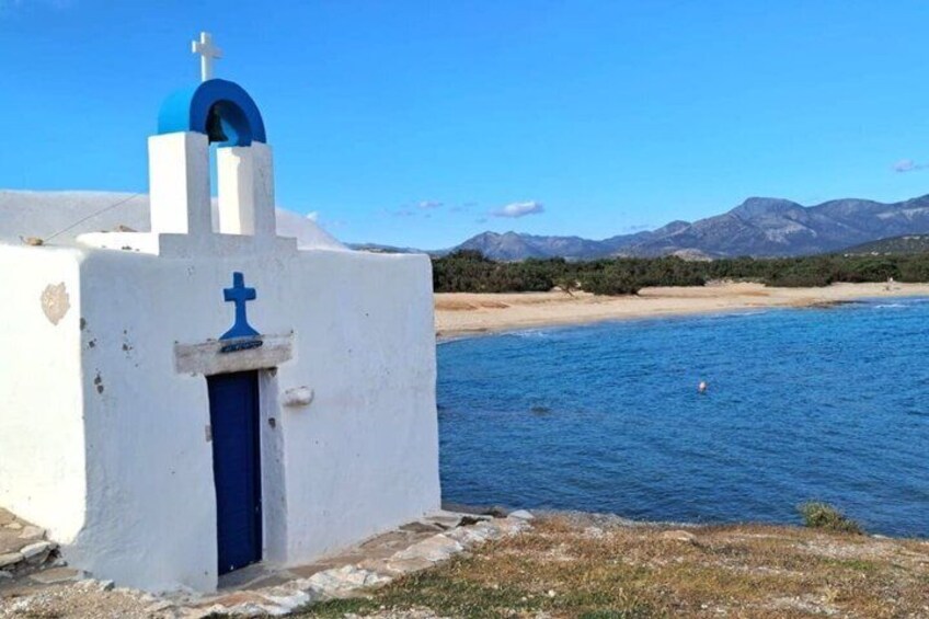 A white building with a blue door and cross, a beach, and mountains in the background. 4