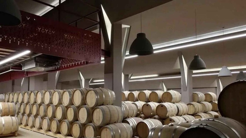 Stacks of wooden barrels in a warehouse with overhead lighting. 1