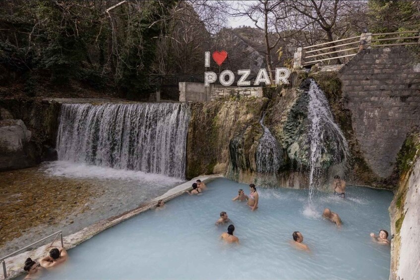 A natural hot spring with multiple waterfalls, surrounded by rocky terrain and trees. 2