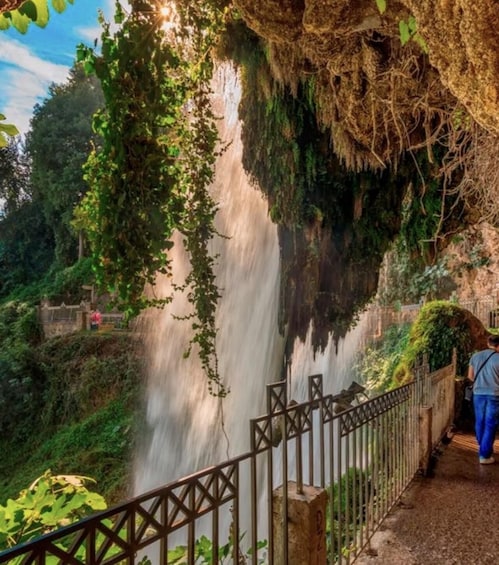 A waterfall cascading over a rocky cliff, surrounded by lush greenery and a metal walkway. 5