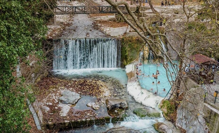 A waterfall cascading into a pool with people swimming, surrounded by greenery and stone structures. 5