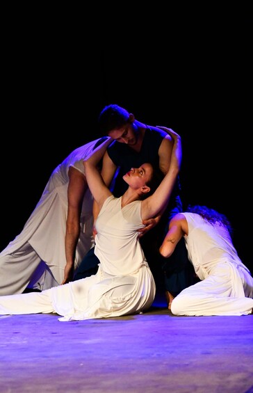 Two people in white costumes performing a dance on a stage with a dark background. 5