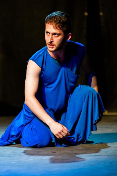 A person in blue attire seated on a stage. 1