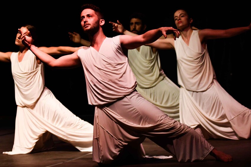 A group of dancers in white and beige costumes performing on a stage. 3