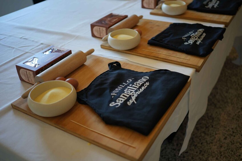 A table with baking tools and a bowl of butter, along with black t-shirts with text. 1