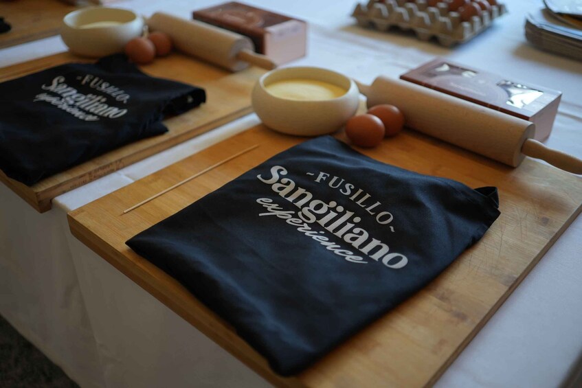 A kitchen counter with cooking utensils, a rolling pin, and two black t-shirts with text. 3