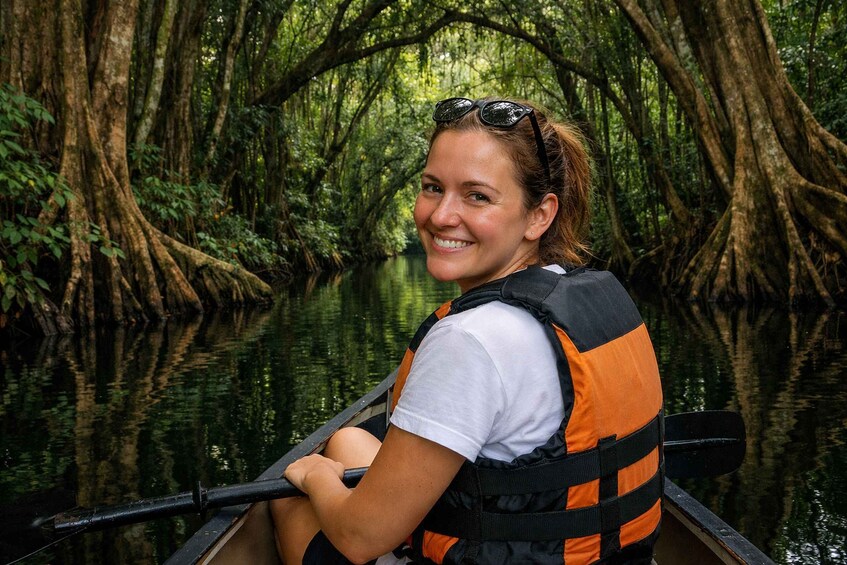 A person in a canoe wearing a life jacket, surrounded by a dense mangrove forest. 2