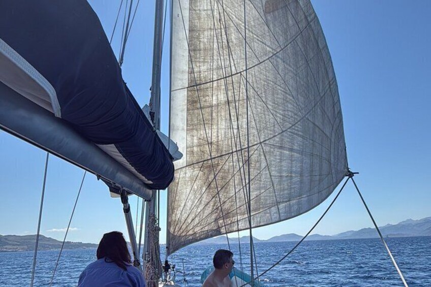 A sailboat with a large sail, two people, and a clear blue sky with distant mountains. 4