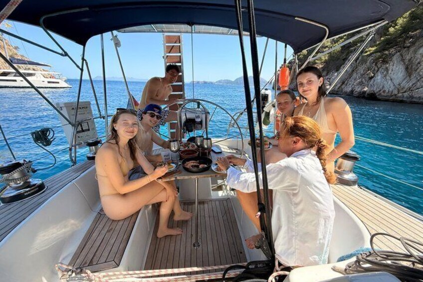 A group of people on a sailboat with a rocky coastline in the background. 1