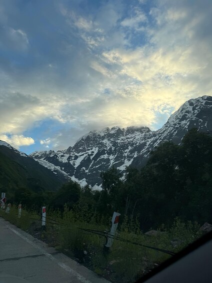 A mountain range with snow-capped peaks, a road with traffic signs, and a cloudy sky. 3
