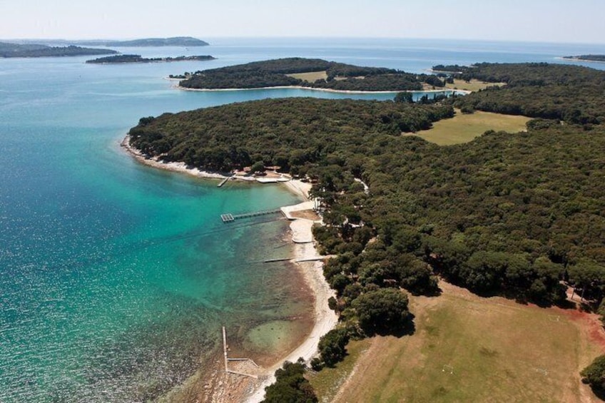 An aerial view of a coastal area with clear turquoise waters, a sandy beach, and a forested peninsula. 4